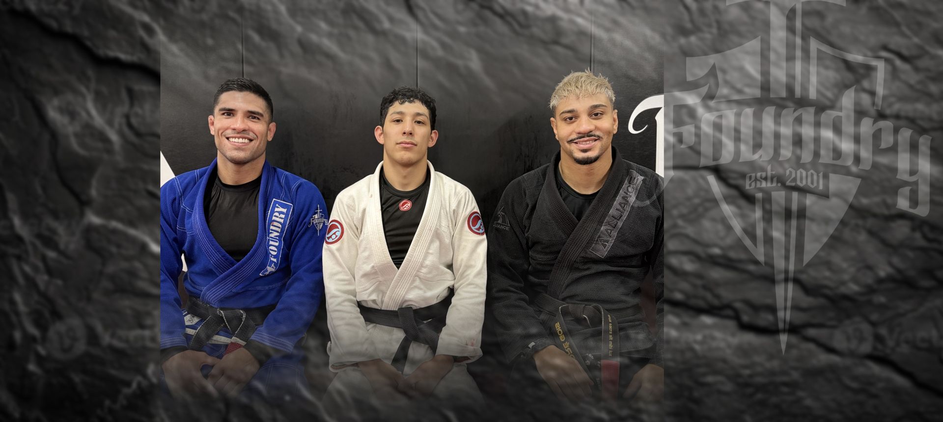 Three men in karate uniforms are sitting next to each other on a rock.