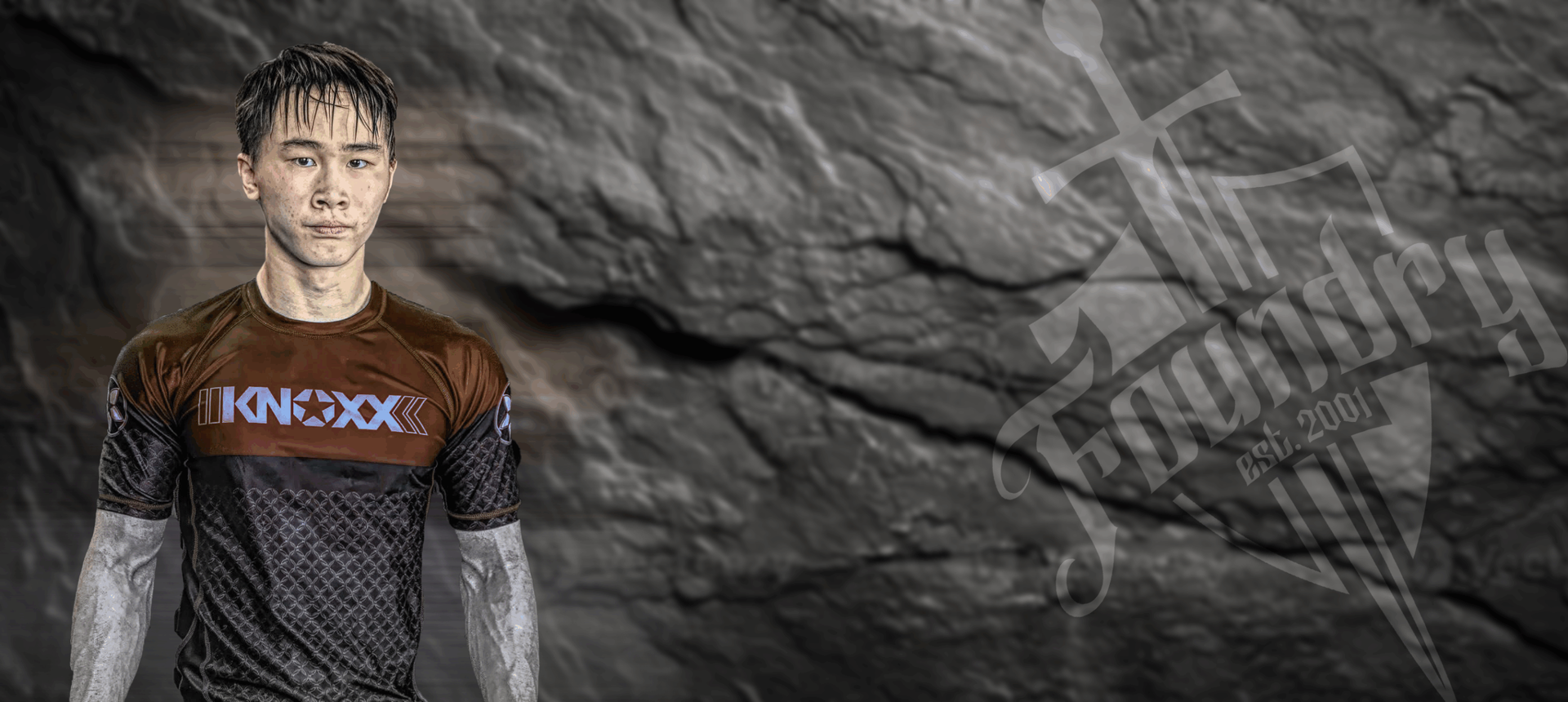 A man is standing in front of a rock wall wearing a rash guard.