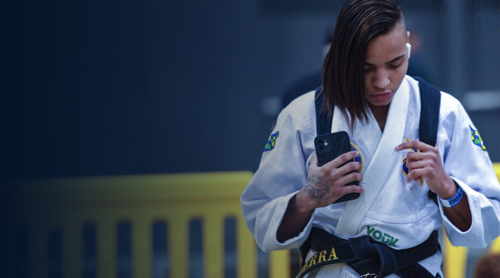 A woman in a karate uniform is looking at her phone.