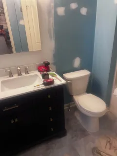 Bathroom under renovation with dark vanity, teal walls, and white toilet.