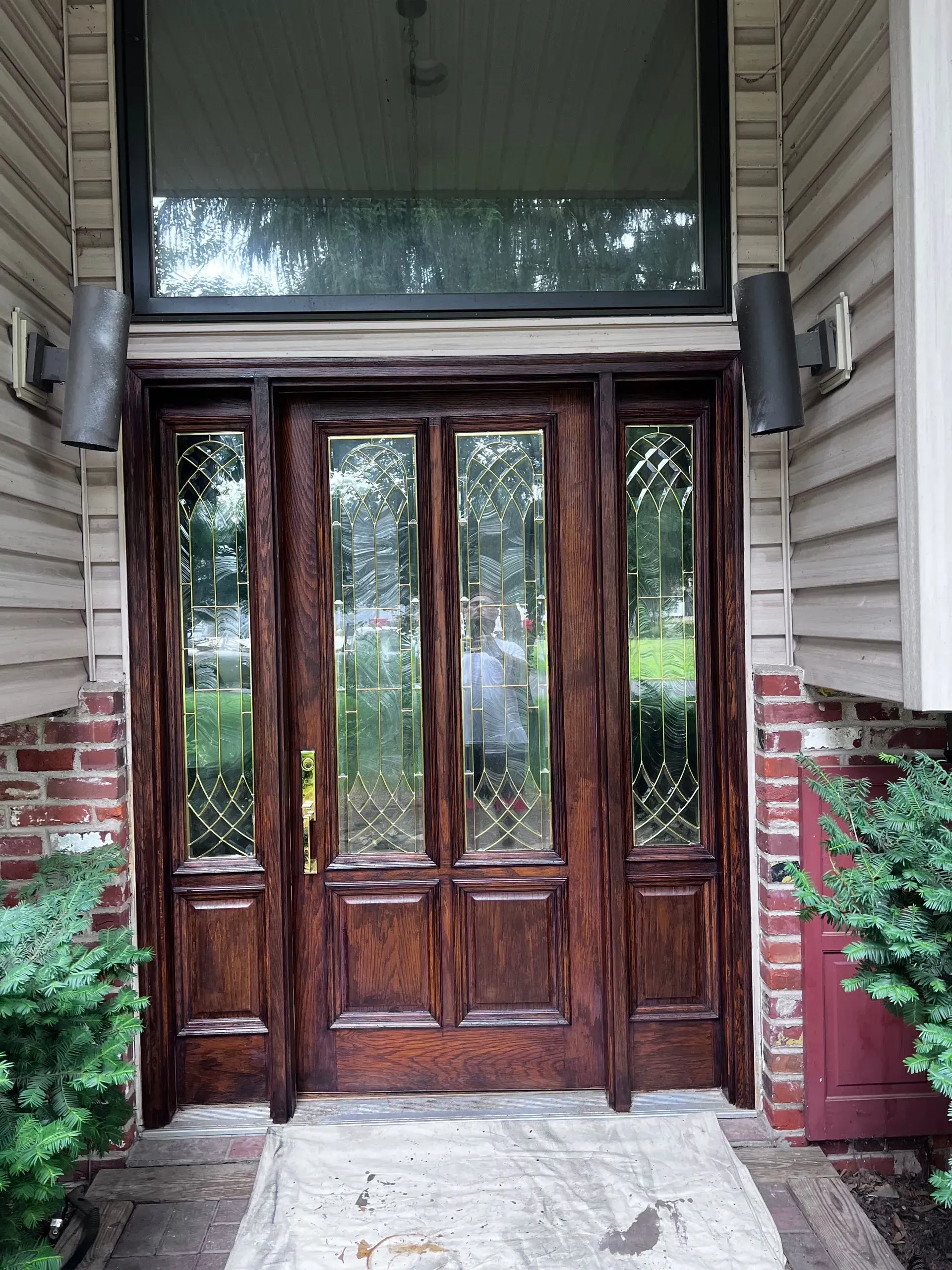 Wooden front door with glass panels and sidelights under a large transom window. Two outdoor lights on either side.