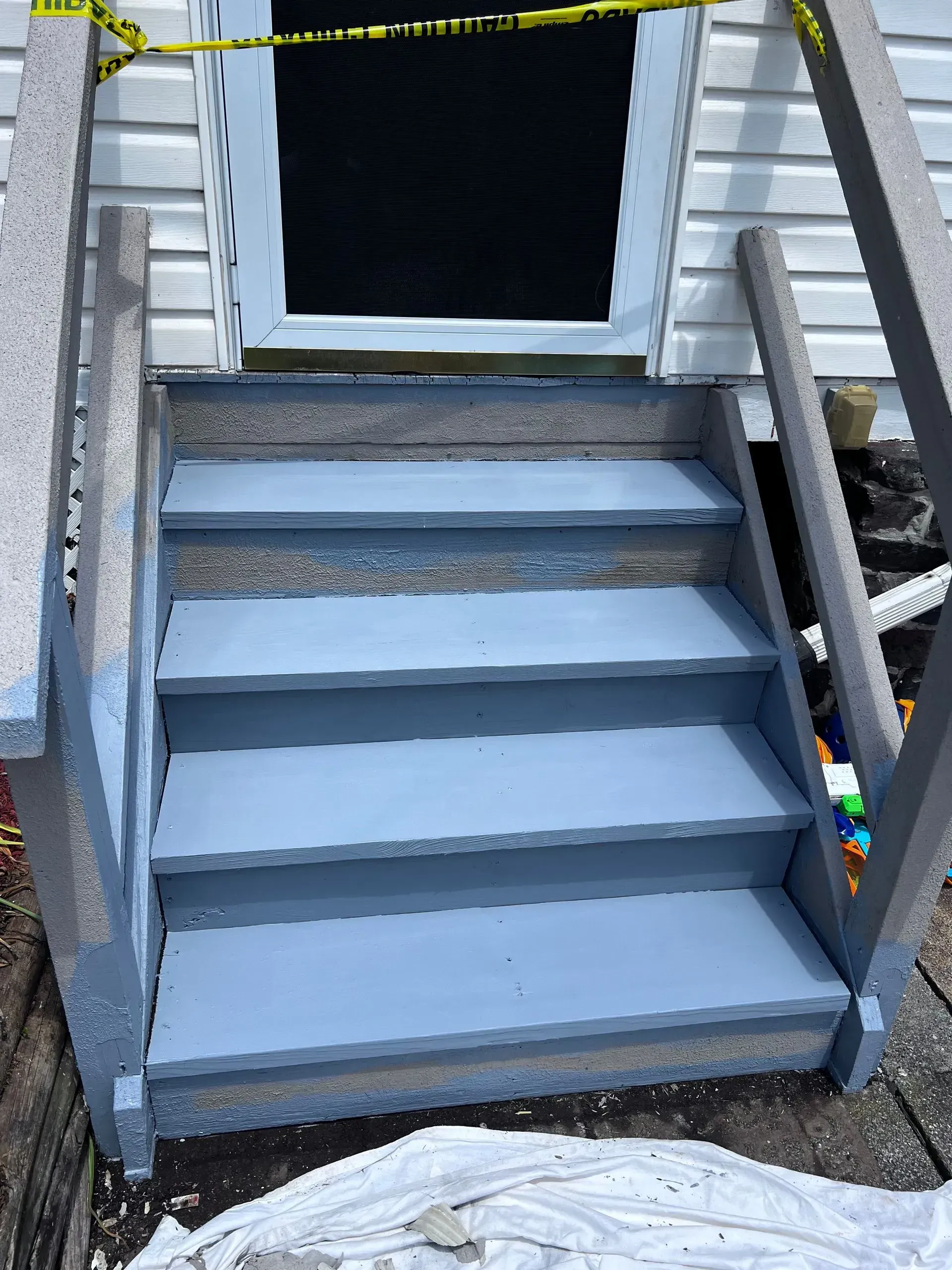 Four light-blue painted steps lead to a door taped off with yellow caution tape; gray handrails.