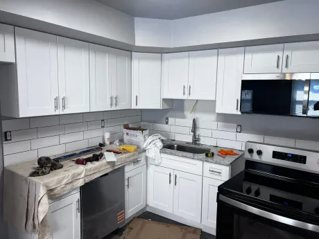 White kitchen cabinets and appliances; countertops and backsplash are being installed.