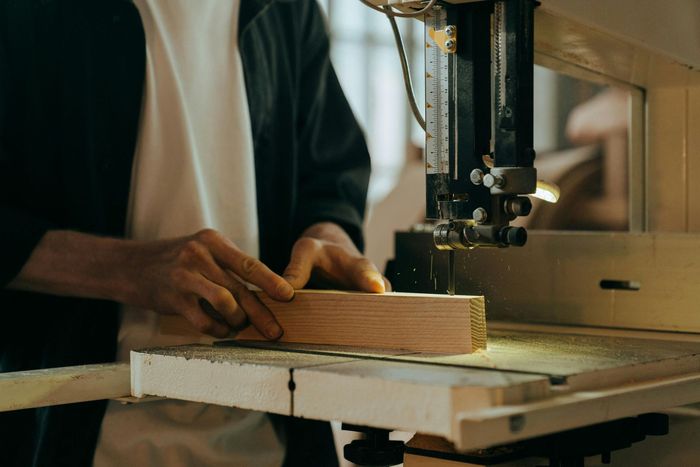 Person using a band saw to cut a piece of wood in a workshop.