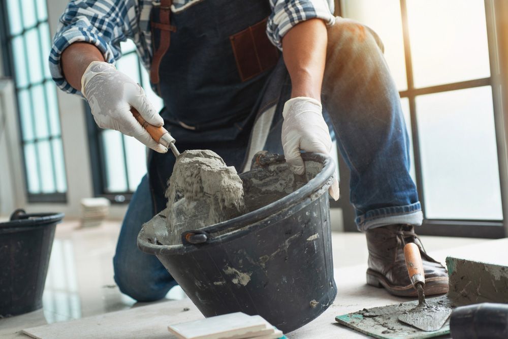 A Man Is Kneeling Down With A Bucket Of Cement And A Trowel — Skilled Transport Training And Assessment in Woongarrah, NSW