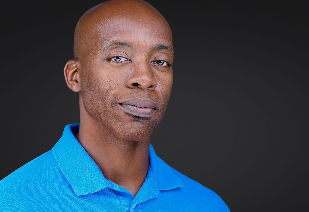 A bald man in a blue shirt is smiling for the camera.