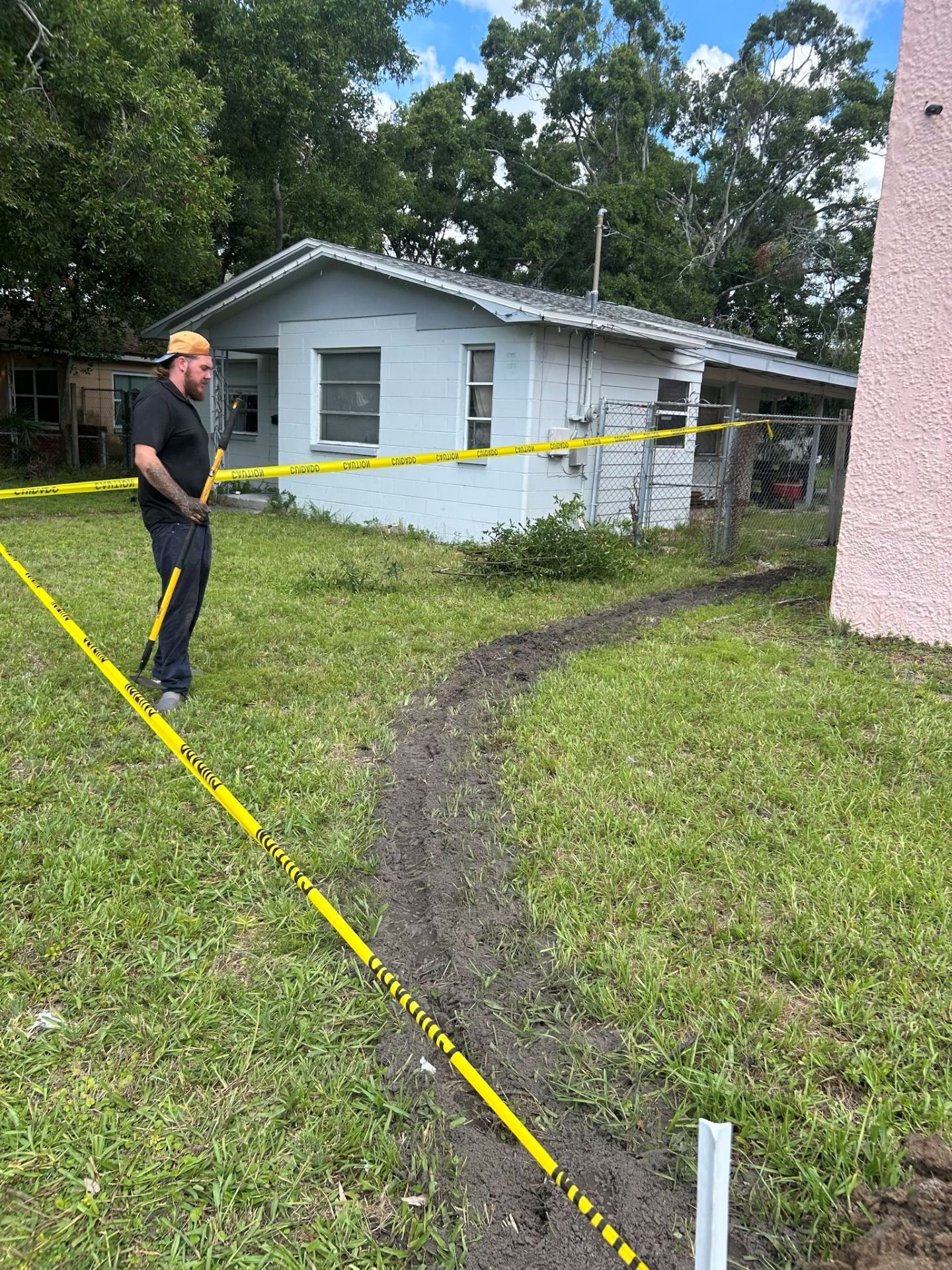 A person in black clothing near a small, light-colored house marked with yellow caution tape, overcast sky.