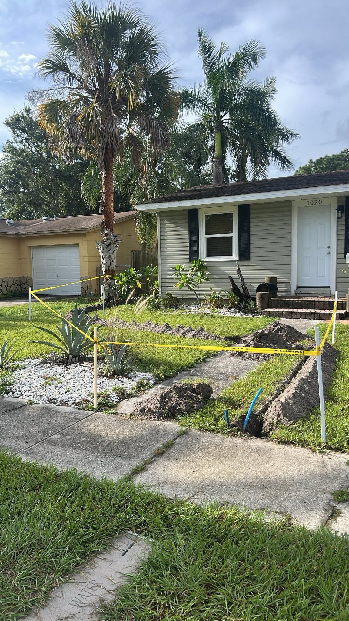 House with yard roped off, concrete walkway. Trees and garage in background. Green grass.