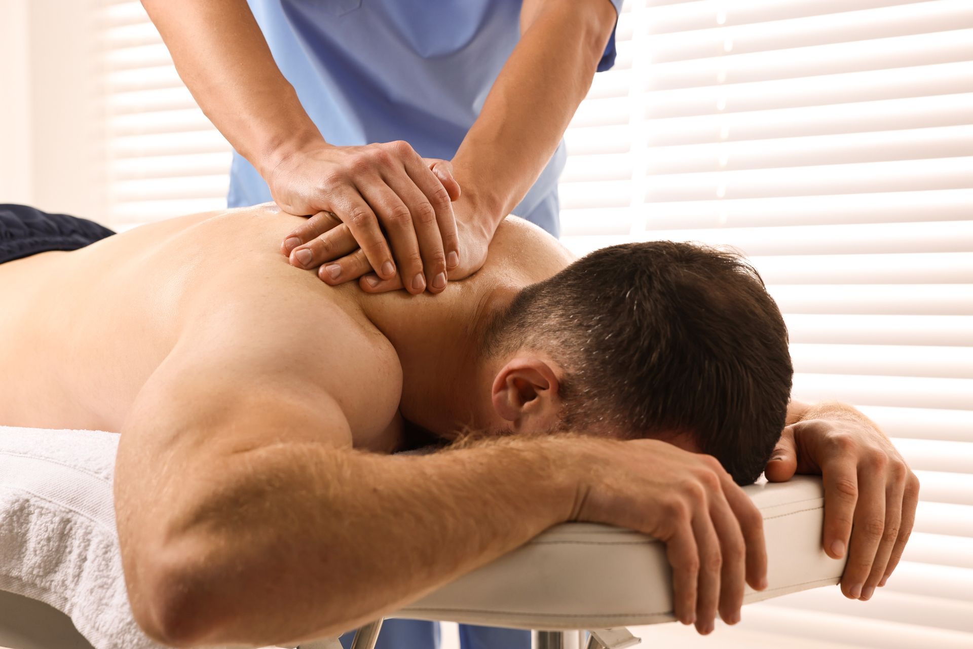 Massage therapist kneading a man's back on a massage table in a bright room