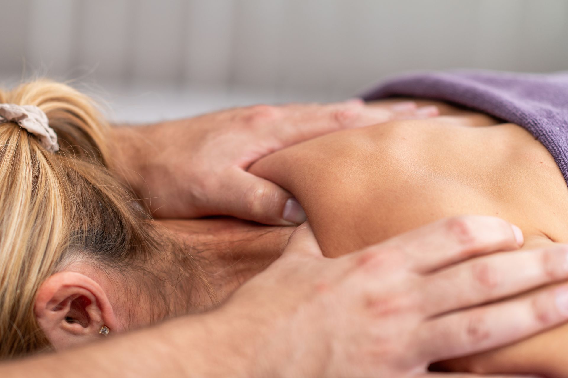 Person receiving a shoulder massage with hands pressing on the upper back, covered by a purple towel.
