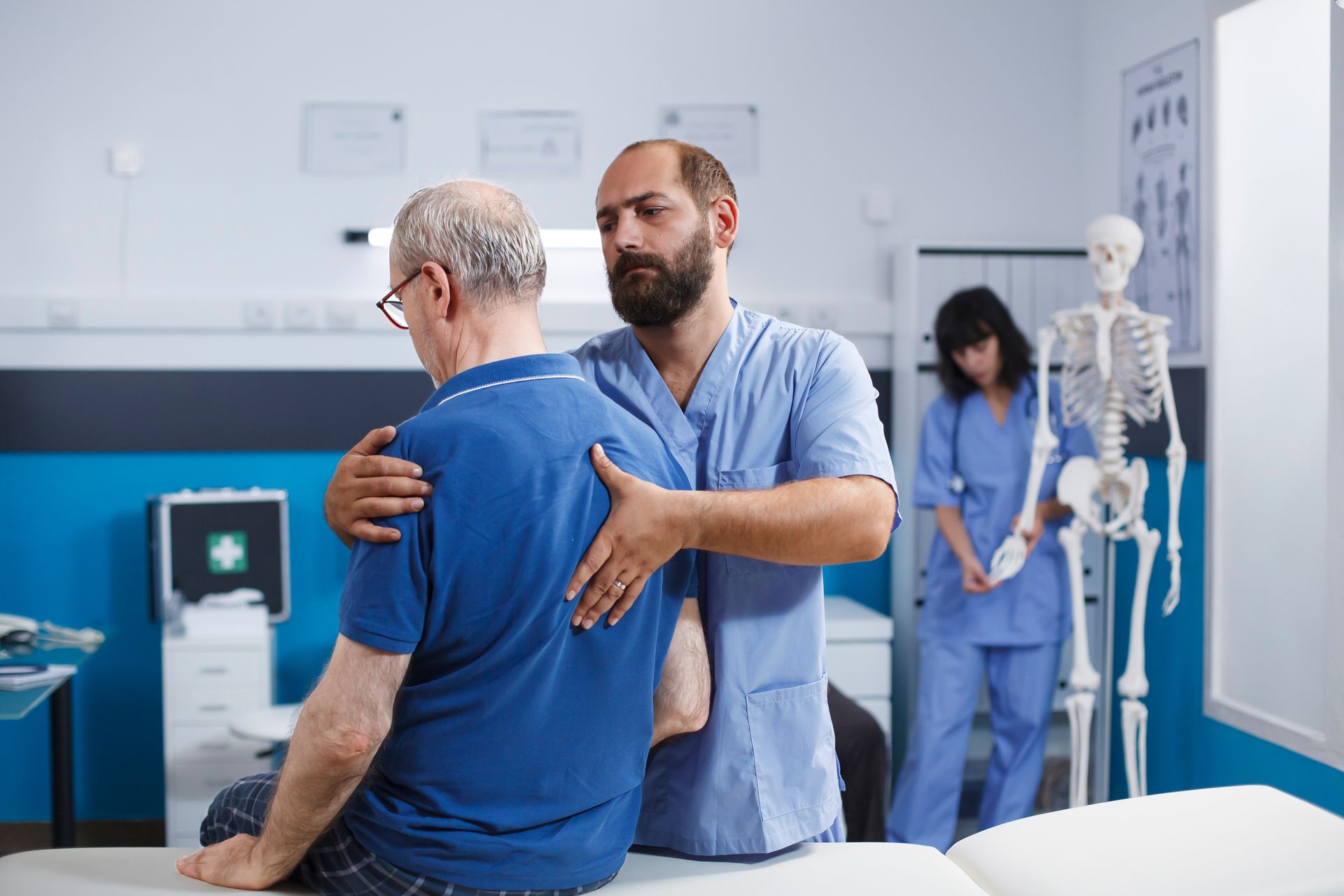 Physical therapist assisting a patient with shoulder exercises in a clinic, with medical staff and skeleton model nearby