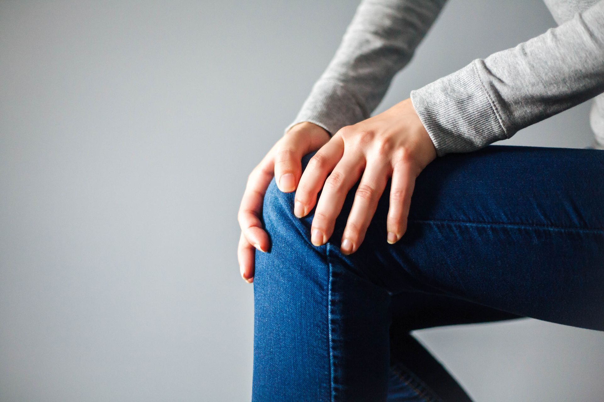 Hands resting on a bent knee in blue jeans and a gray sweater.