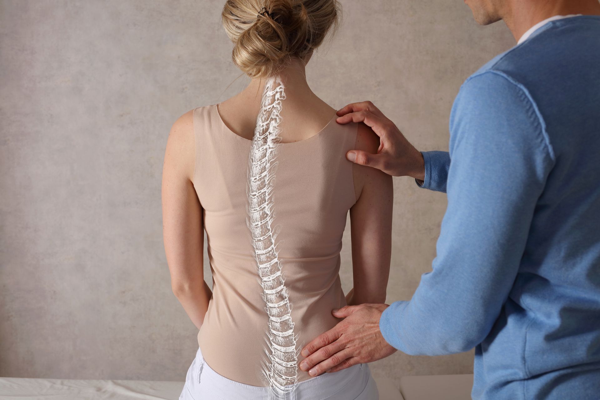 Physical therapist examining a woman's spine while she stands against a neutral background