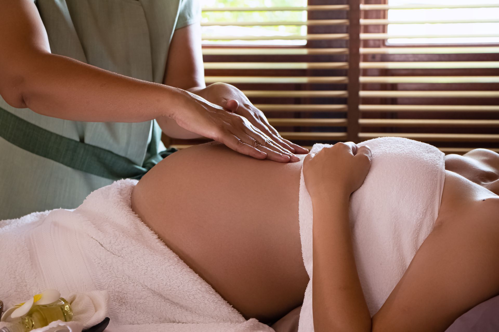 Person lying on a bed with hands on a pregnant belly, wrapped in a white towel.
