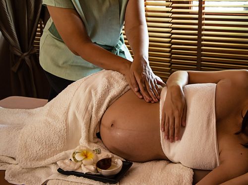 Pregnant person receiving a relaxing massage while lying on a bed in a calm spa setting