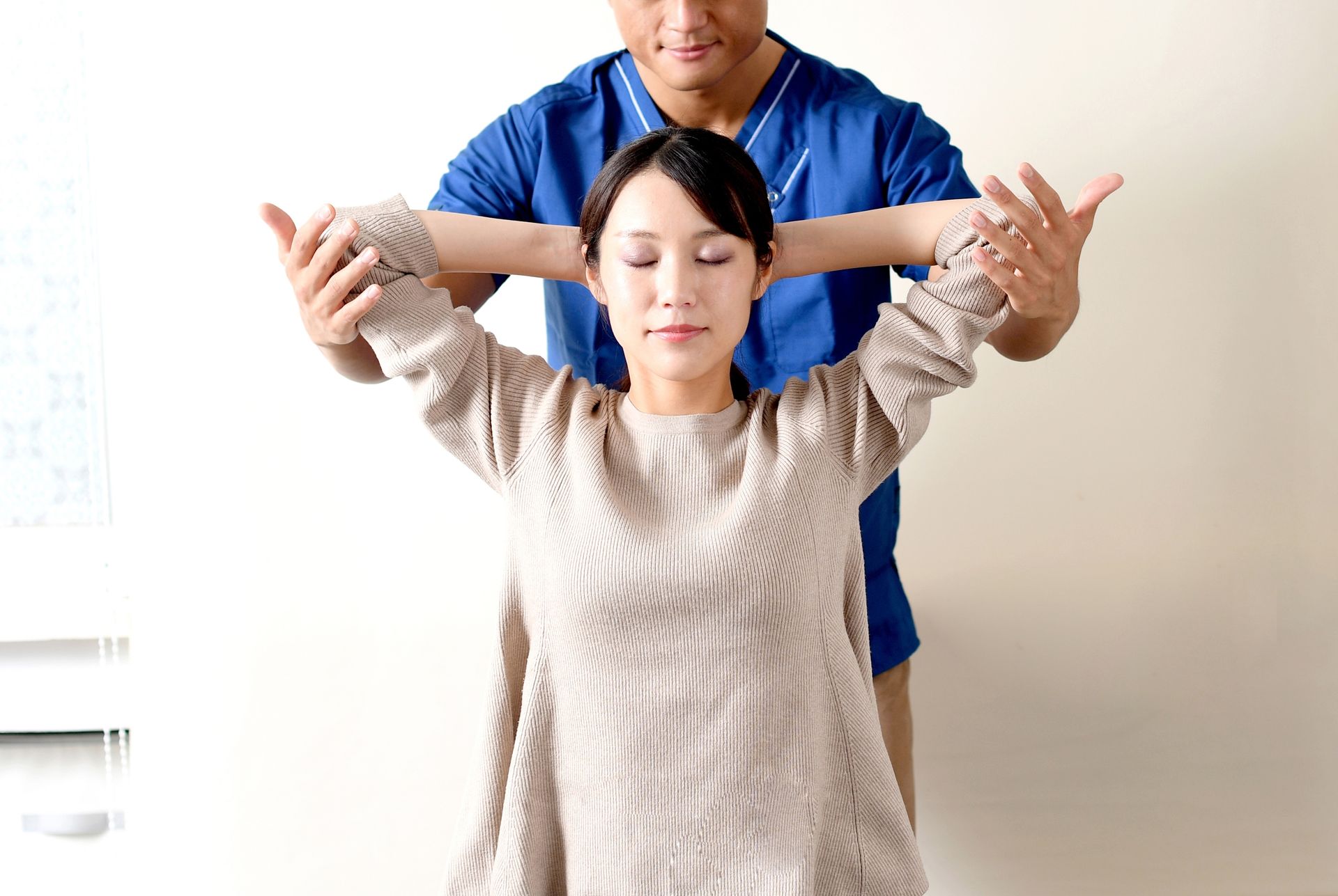 Person assisting another with a shoulder stretch in a bright room