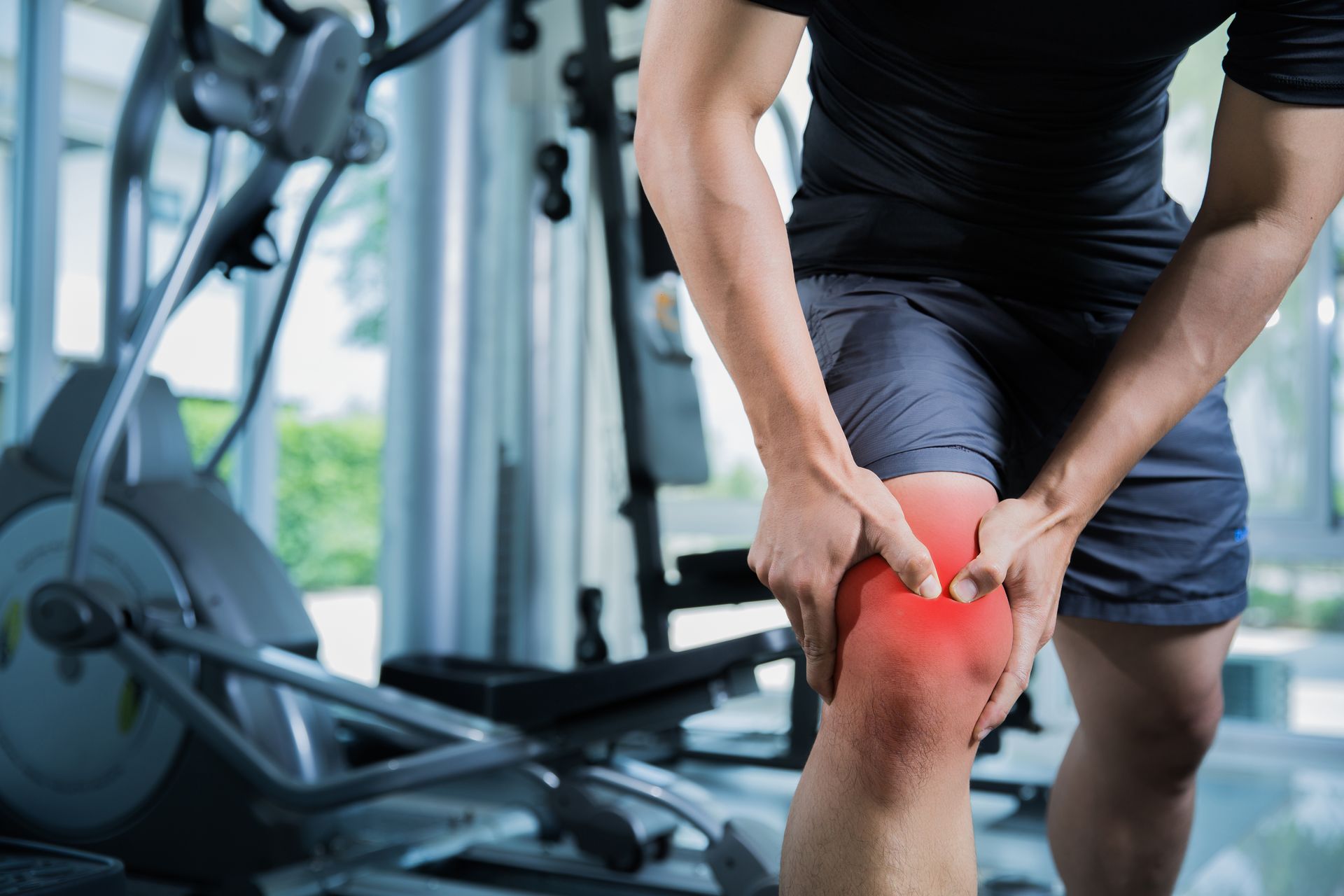Person clutching a red, painful knee in a gym, suggesting an injury or strain