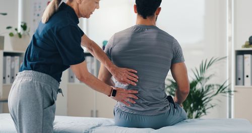 Therapist helping seated client with back massage in a bright clinic room