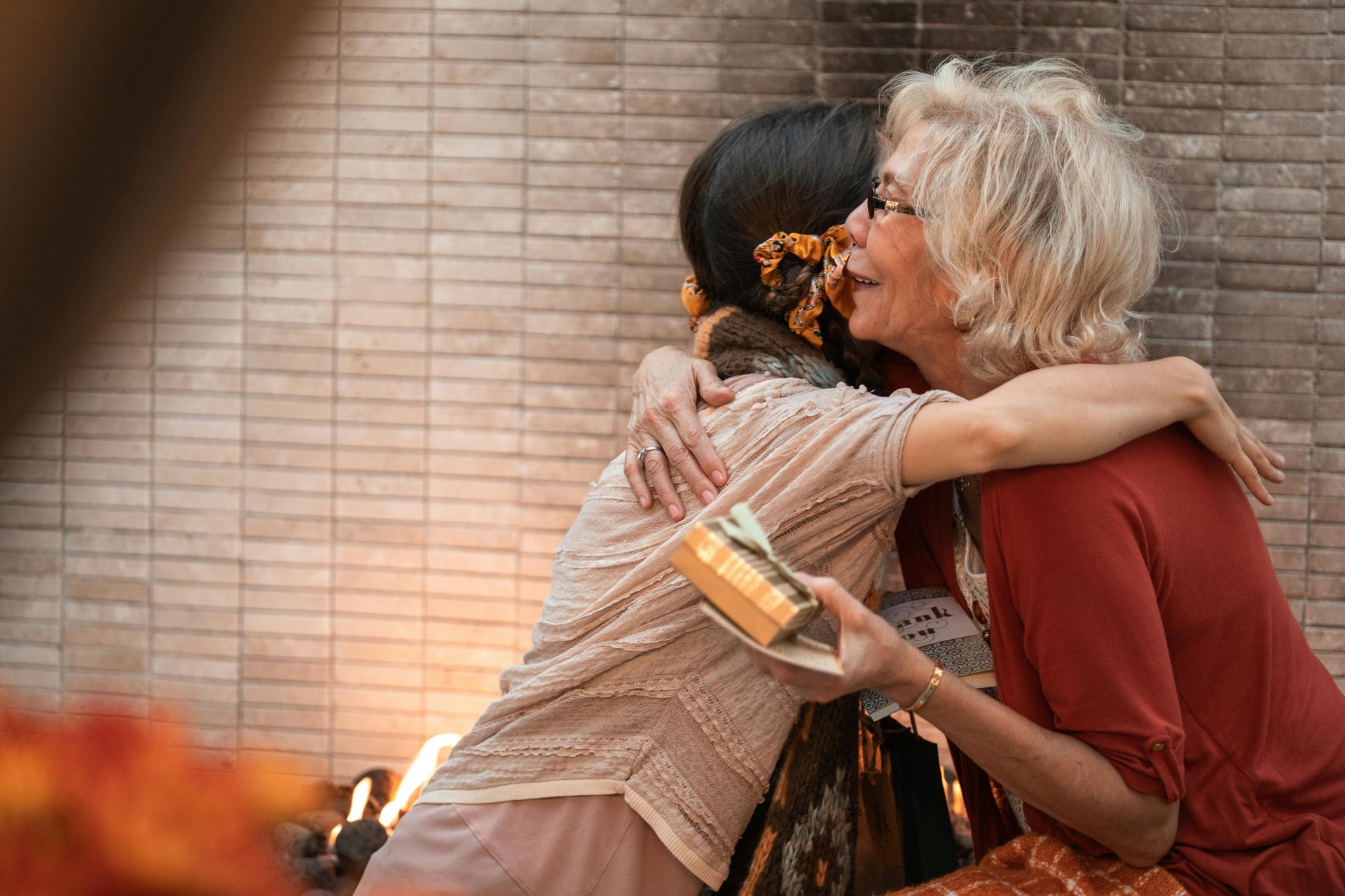 Two women are hugging each other in front of a fireplace.