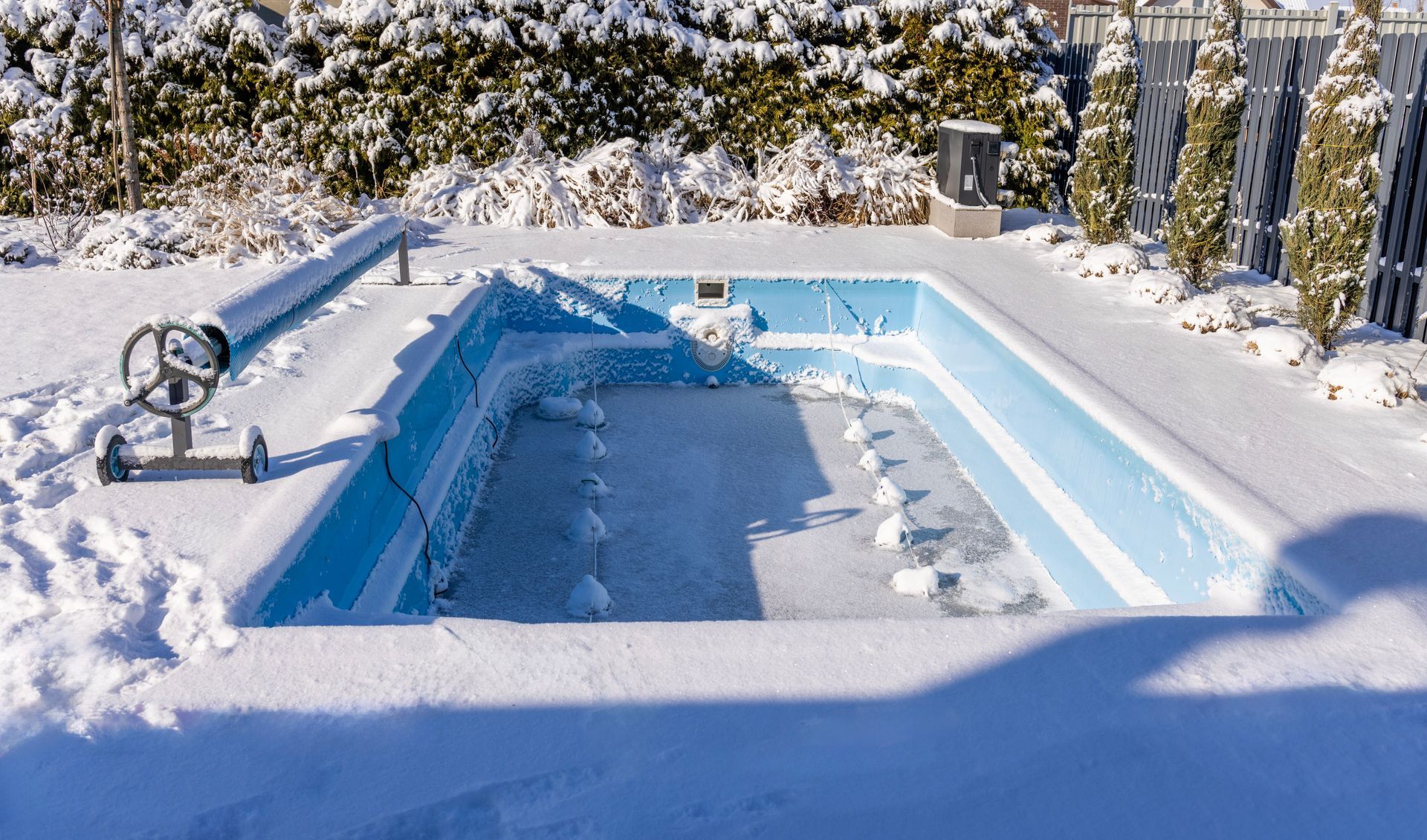 Eine Person reinigt ein leeres, rechteckiges Schwimmbecken. Das Becken hat eine beige Innenfläche und eine dunkle Abdeckung.