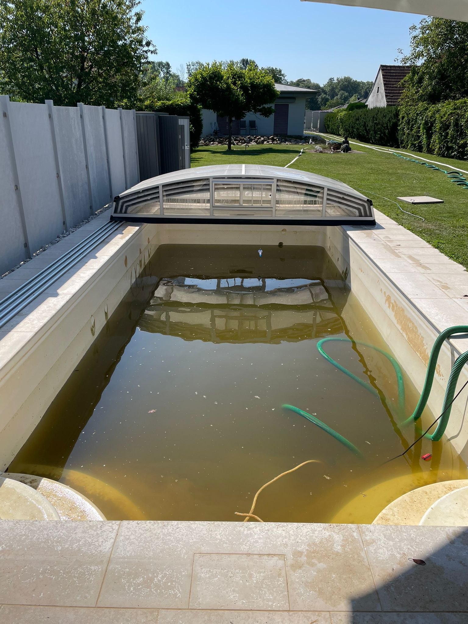 Schmutziger, algenreicher Pool mit teilweise geöffneter Abdeckung in einem Hinterhof.