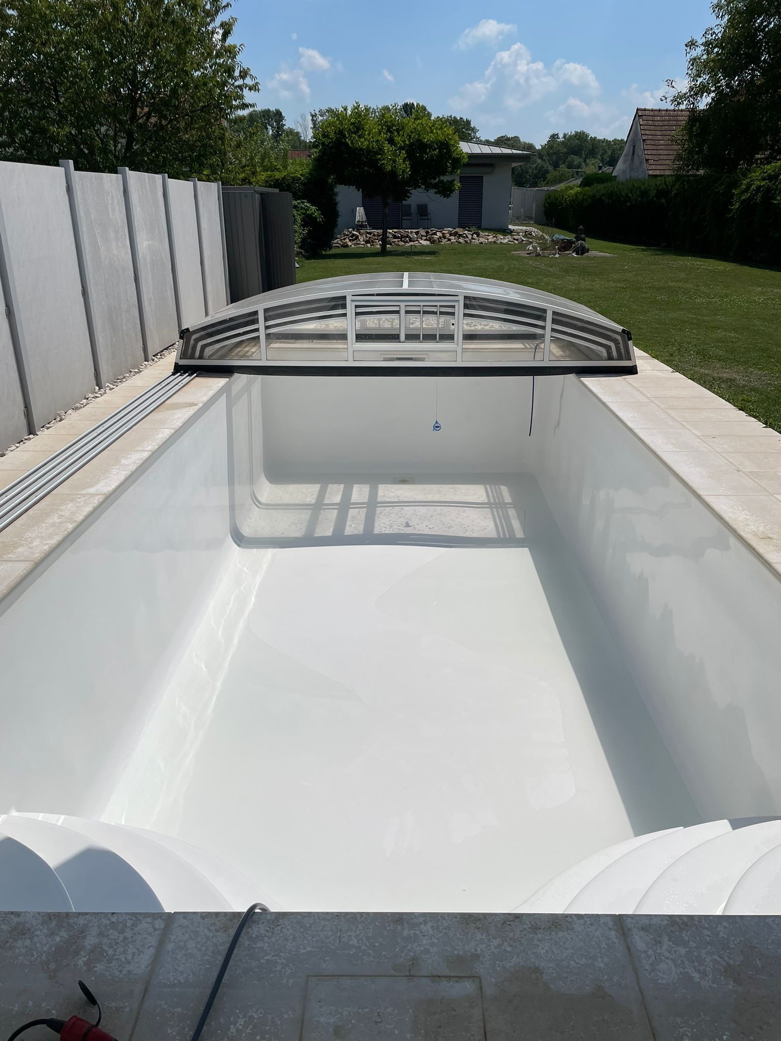 Leerer rechteckiger Swimmingpool mit einziehbarer Abdeckung unter blauem Himmel.