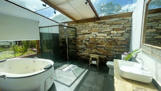 Quarto espaçoso com uma plataforma de madeira elevada que sustenta uma cama, teto com painéis de madeira e grandes janelas com vista para o exterior.