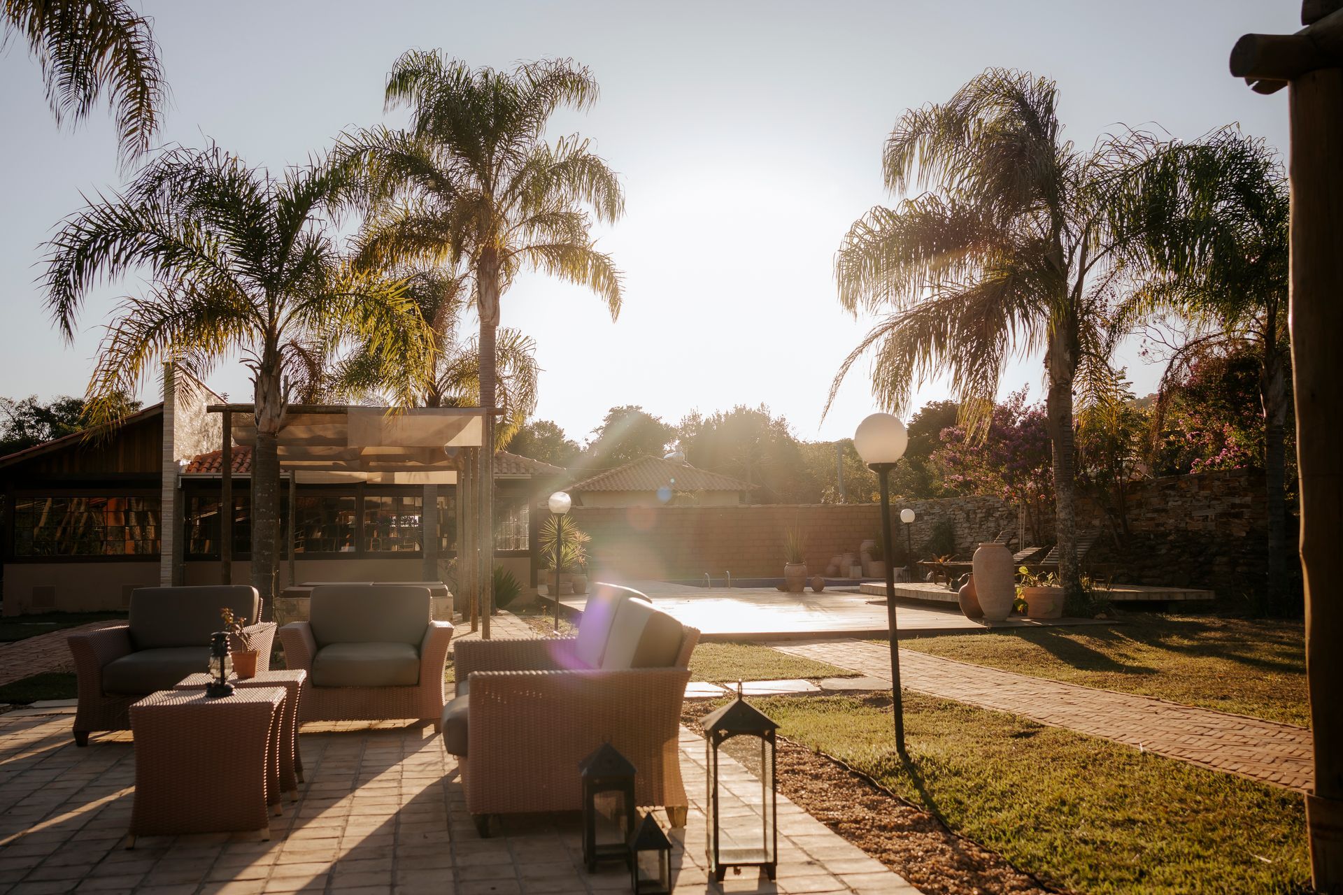 Um pátio ensolarado com assentos confortáveis, palmeiras altas e iluminação externa ao pôr do sol.