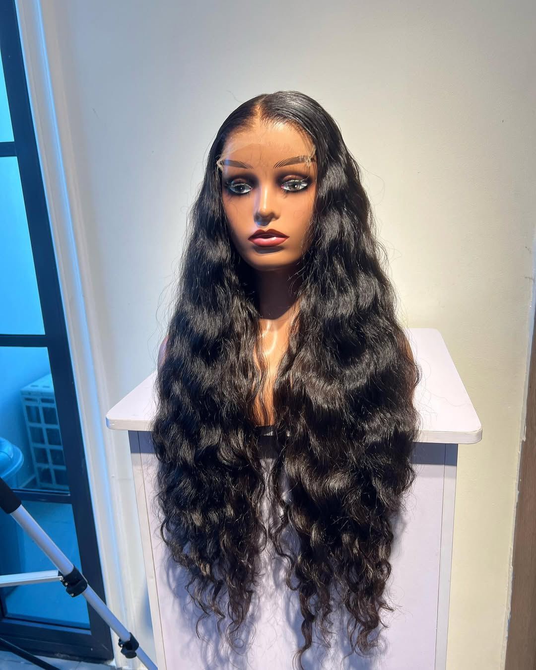 Peluca negra ondulada sobre una cabeza de maniquí, expuesta sobre una superficie blanca