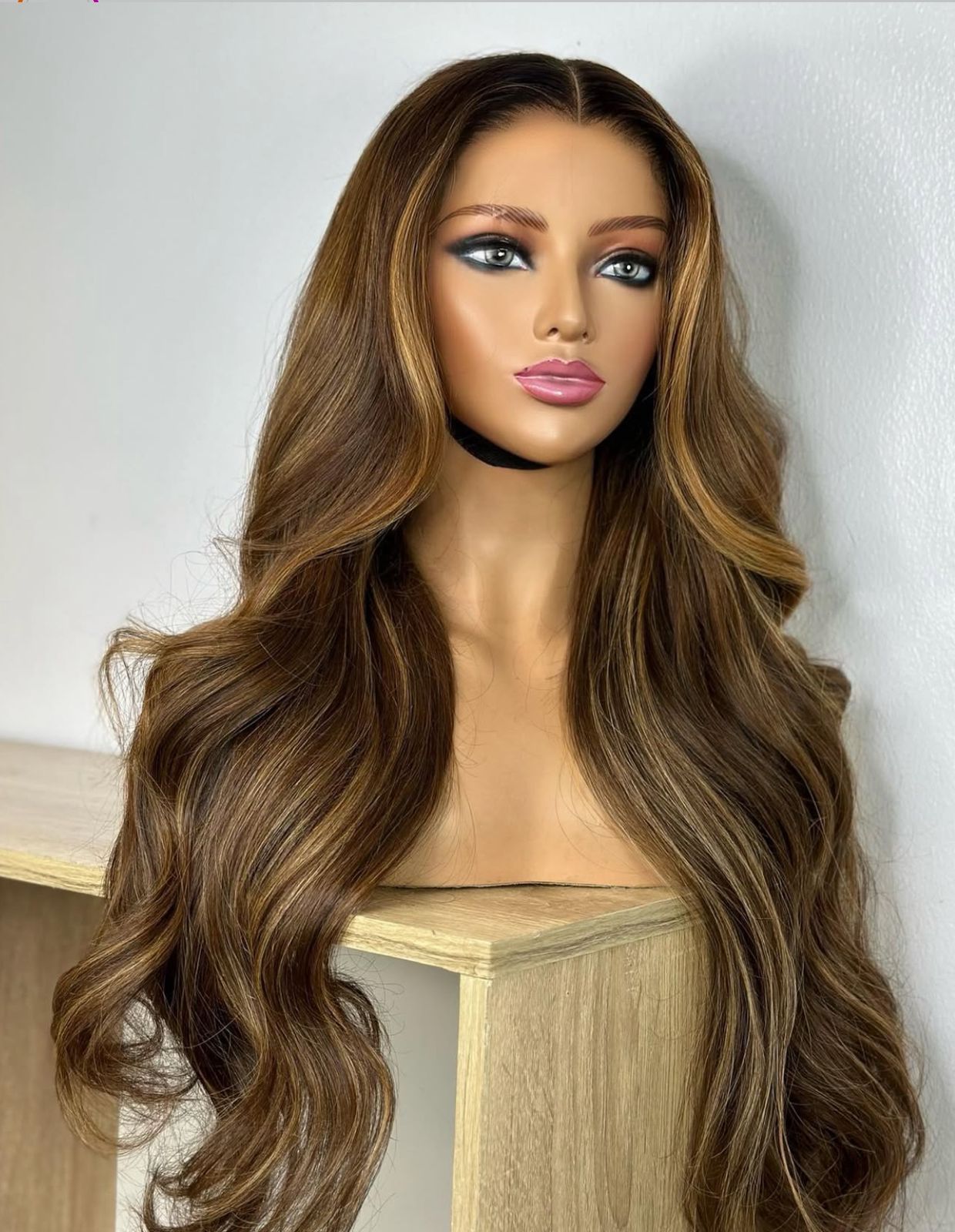 Cabeza de maniquí con peluca larga y ondulada de color marrón con reflejos rubios.