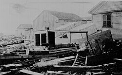 Black and white historical photo showing debris and damaged wooden buildings in the aftermath of a flood or storm.