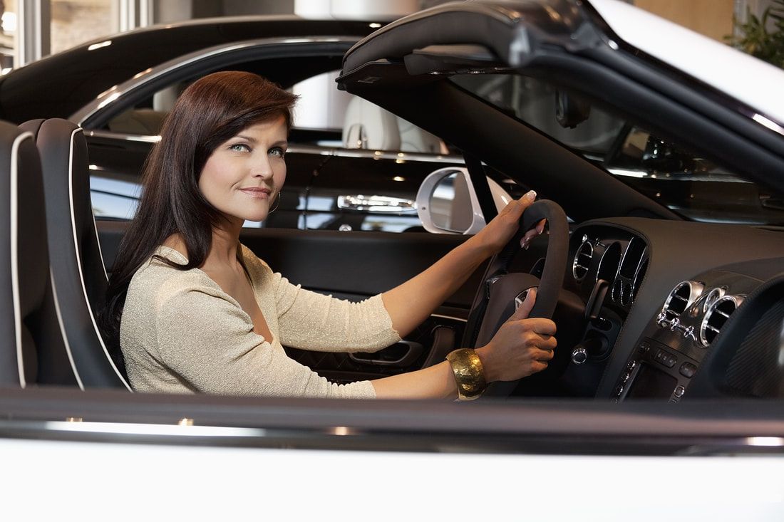 Woman sitting in a white convertible car, smiling.