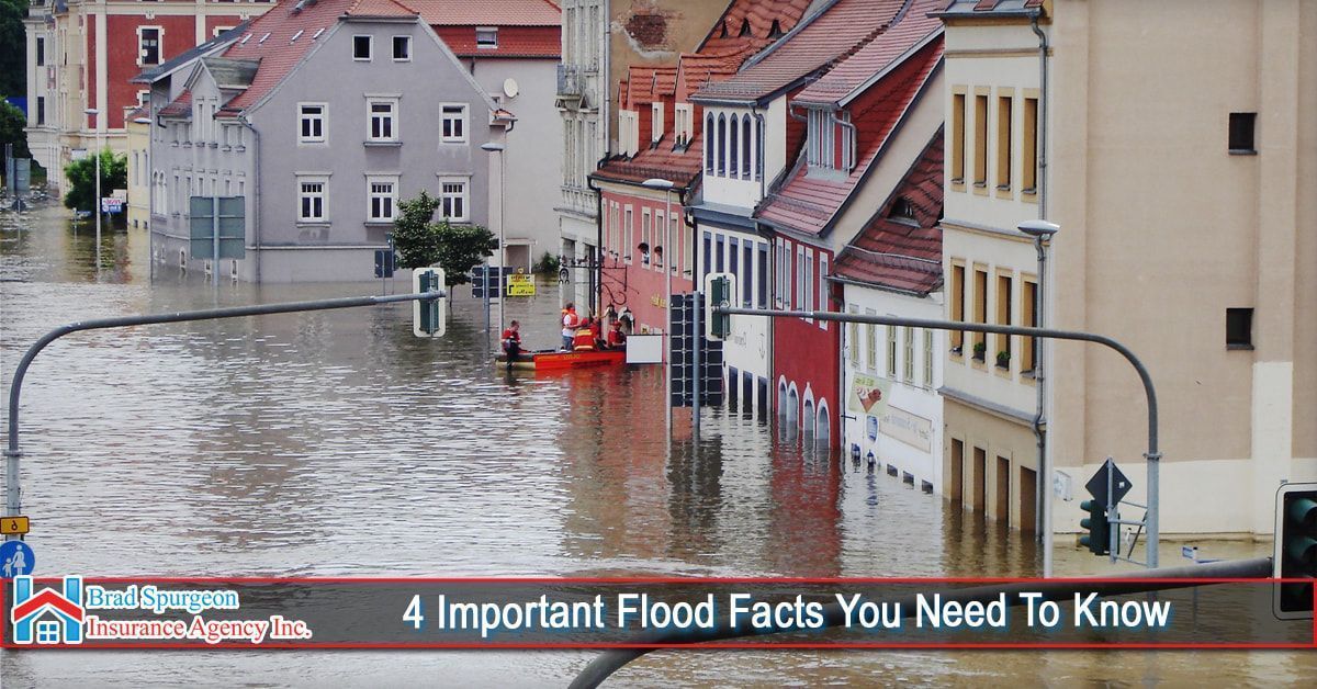 Floodwaters submerge a city street between buildings, with rescuers in a small orange boat navigating the current.