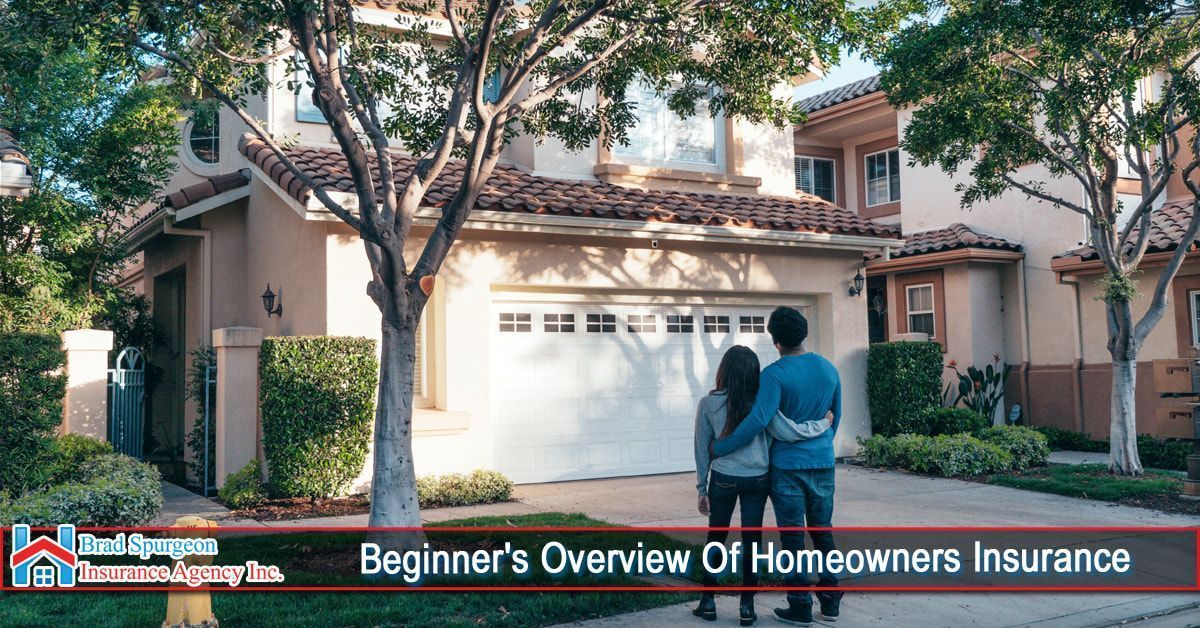 A couple stands in a driveway looking at a tan, two-story house with a white garage. 