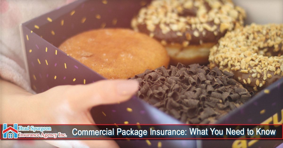 A person holds a box of four donuts with varied toppings