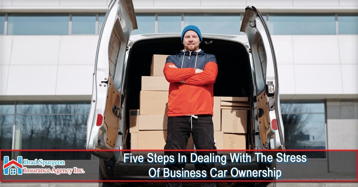 A person stands with arms crossed in front of a van filled with cardboard boxes