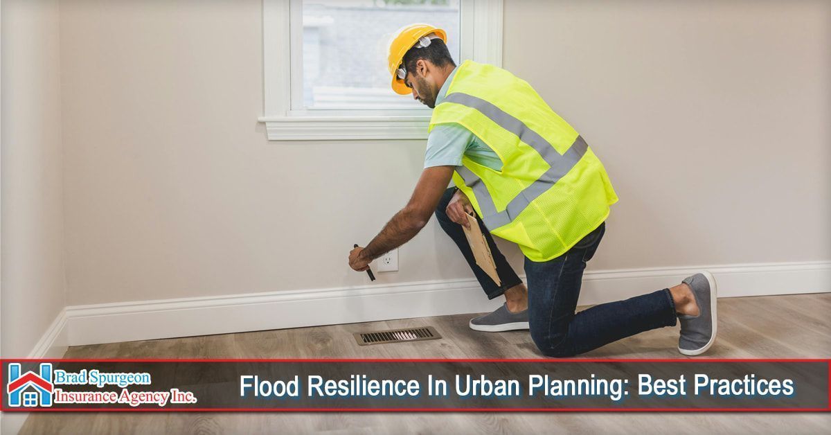 A worker in a yellow safety vest kneeling to inspect an electrical outlet near a floor vent in a room.