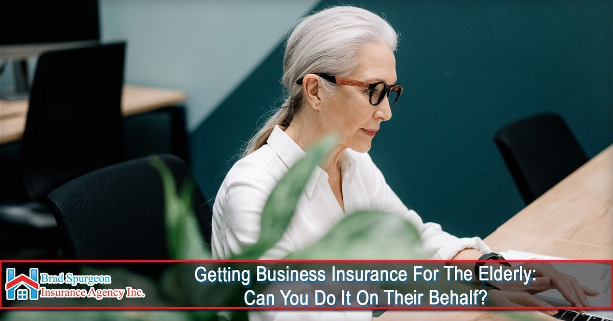 A person with white hair and glasses works at a laptop in an office