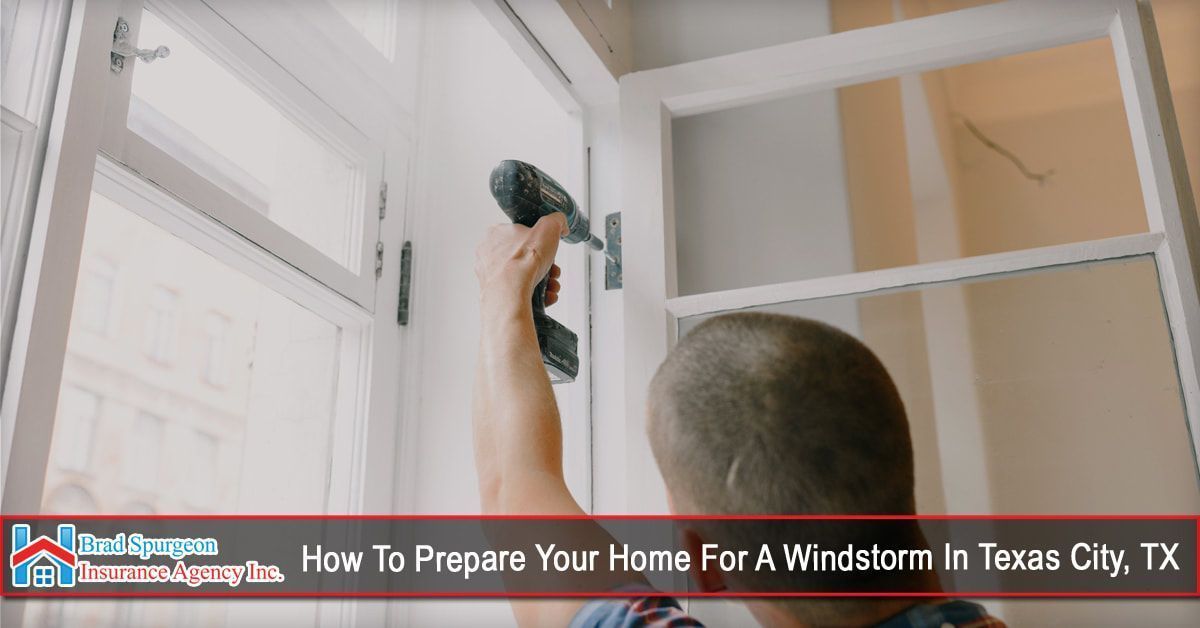 A person using a cordless drill to install a storm shutter on a white window frame.