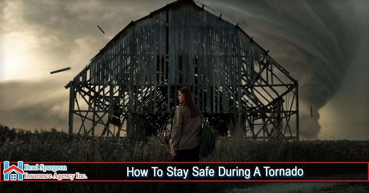 A person stands in a field looking toward a large tornado and a damaged wooden barn