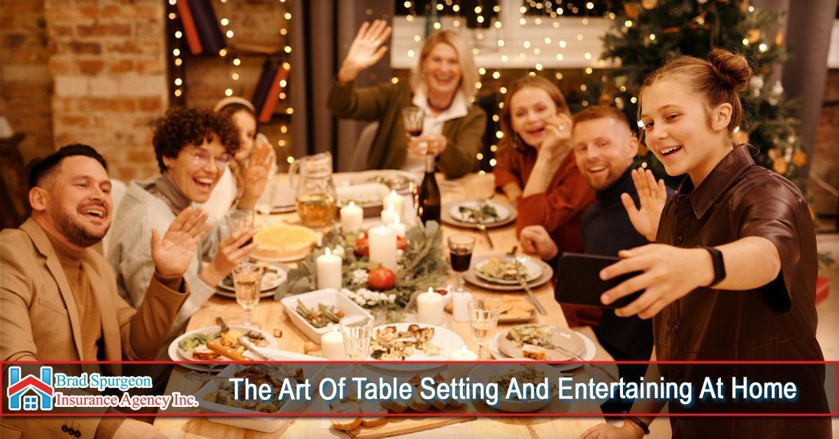 A group of people sitting around a table with food and candles, smiling and waving while taking a selfie together.