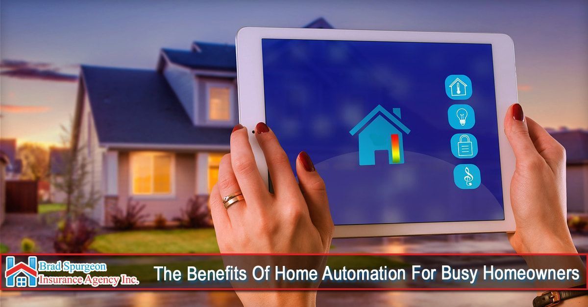 Hands hold a tablet displaying a home automation control interface in front of a house at dusk.