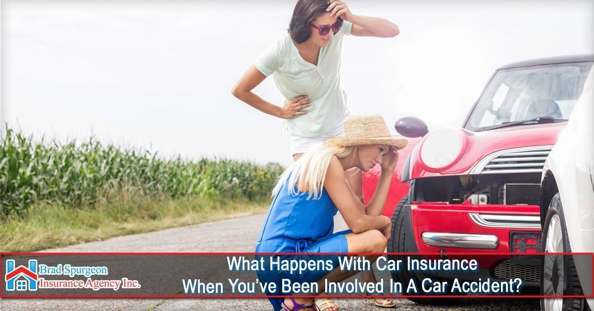Two people look distressed near a red car damaged in a collision on a rural road next to a cornfield.