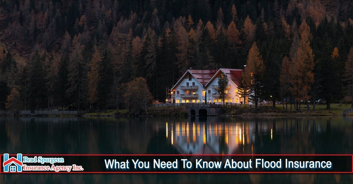 A glowing house sits by a lake surrounded by trees at dusk