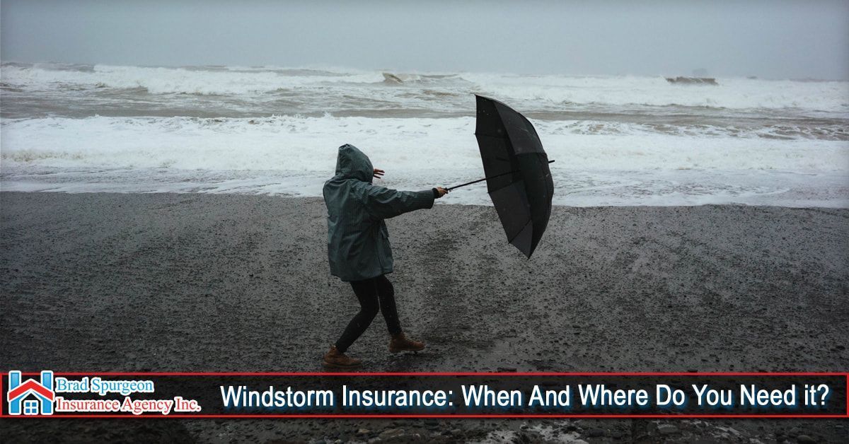 A person in a rain jacket struggles with an umbrella on a beach during a storm