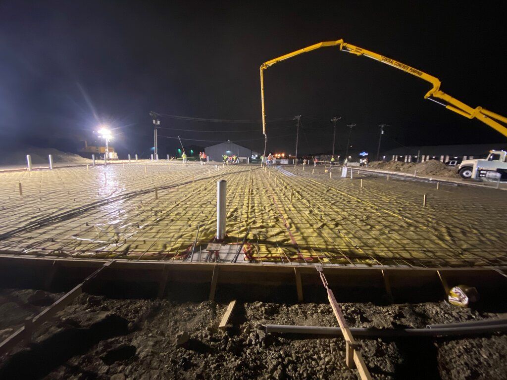 A concrete pump is pouring concrete on a construction site at night.