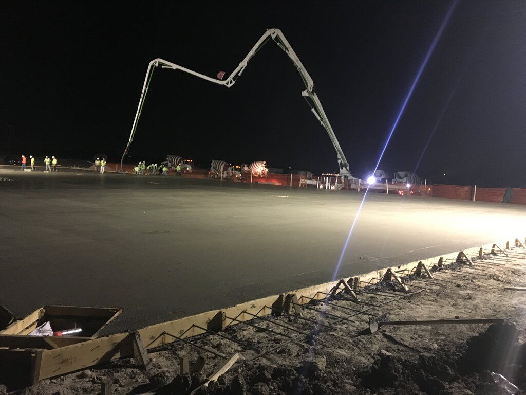 A concrete pump is being used to pour concrete on a construction site at night.