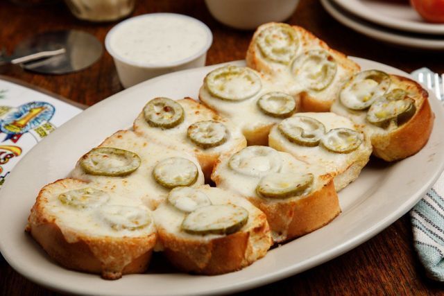 A plate of garlic bread with cheese and pickles on a table.