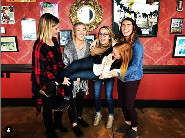 A group of women are posing for a picture and one of them is holding another woman in her arms