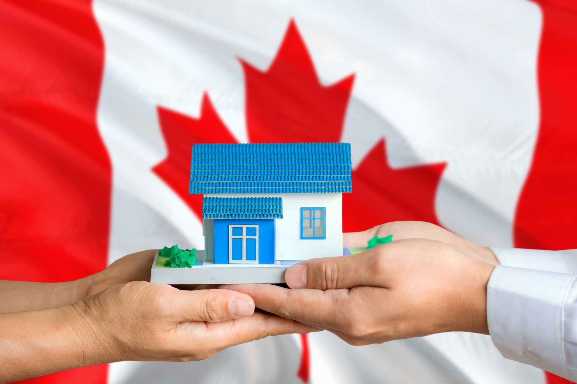 Hands holding a small model house in front of a Canadian flag.